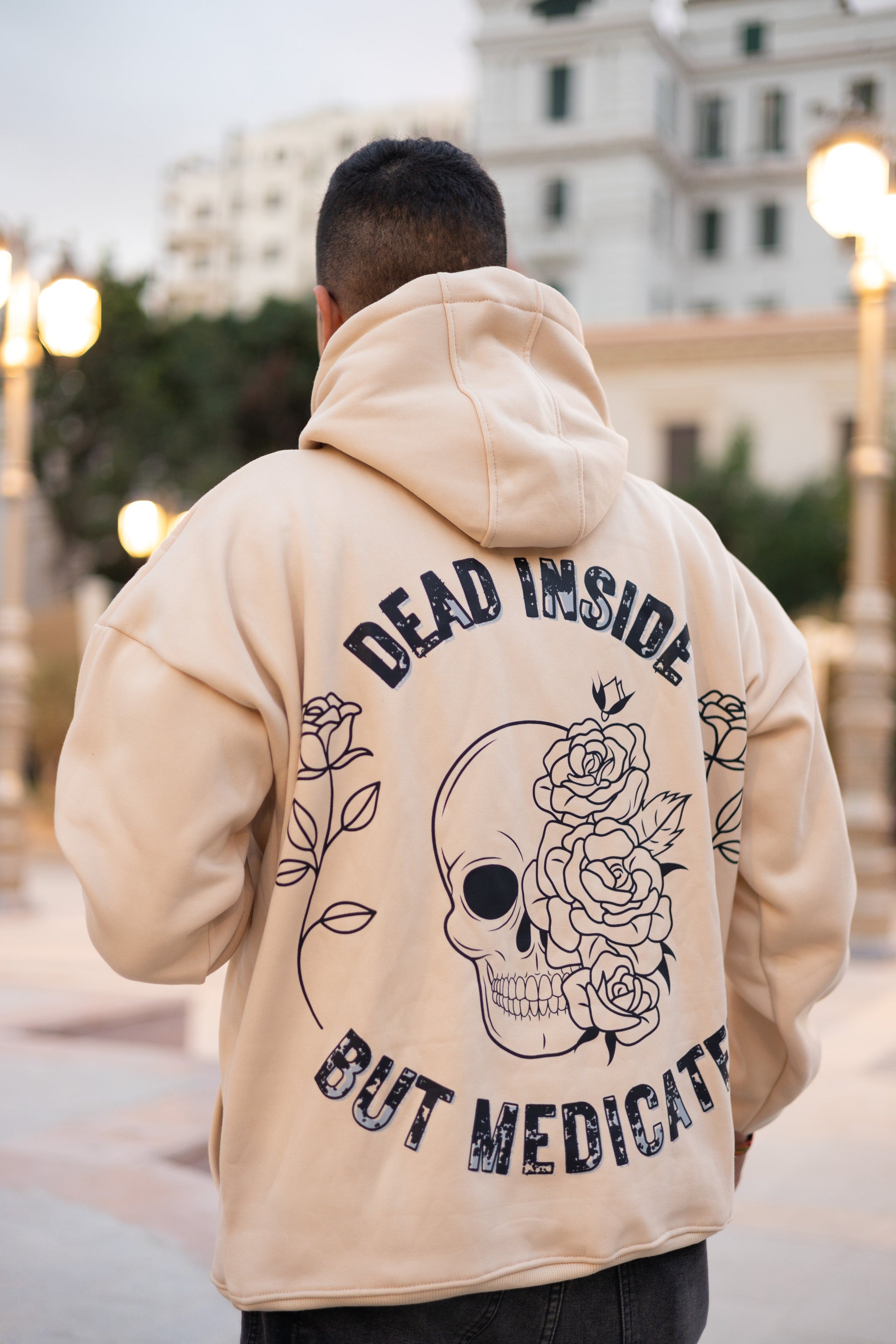 Beige oversized hoodie playing with light and darkness by blending lively roses and creepy skulls balanced with "Dead Inside But Medicated" back caption.