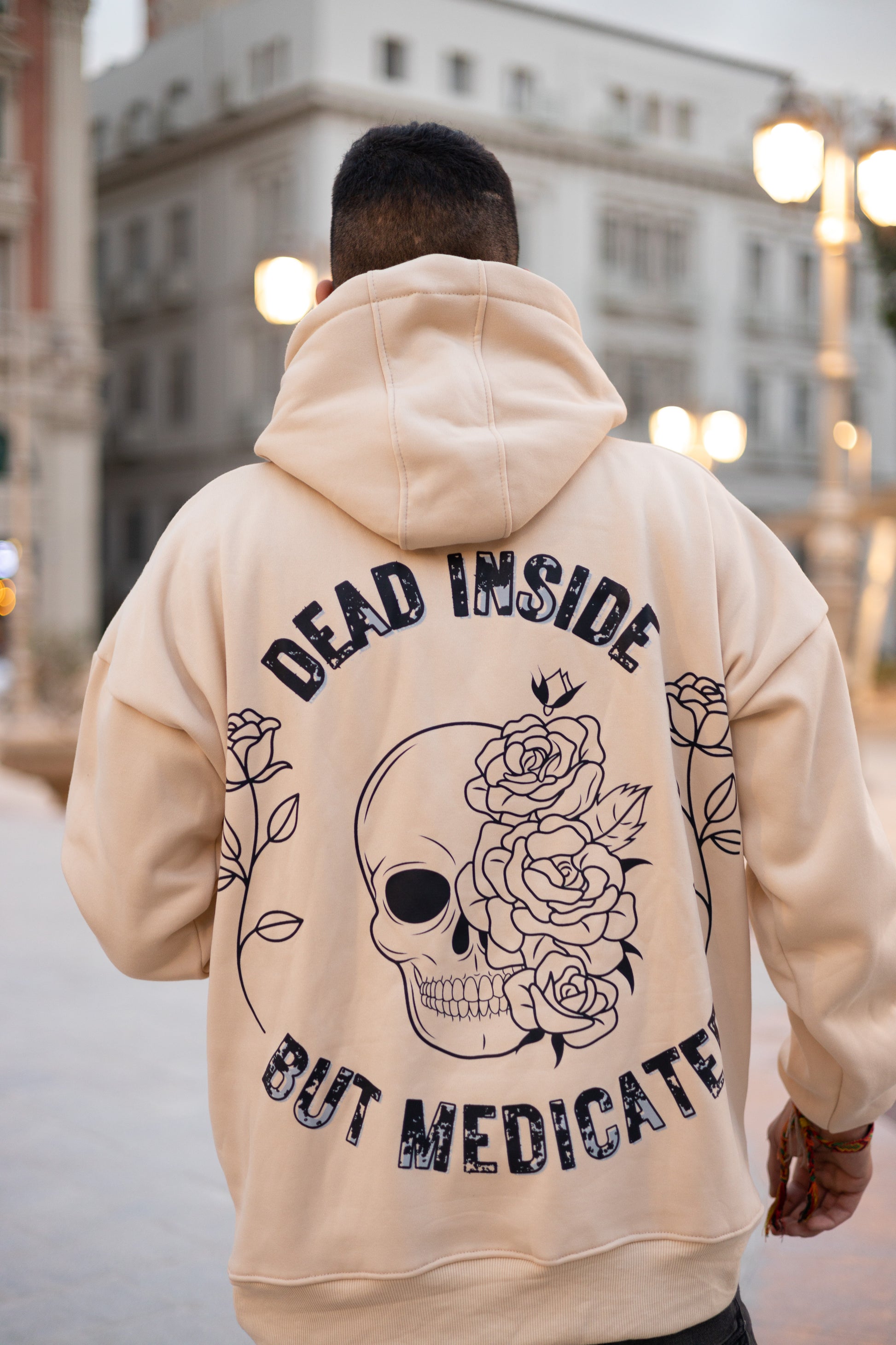 Beige oversized hoodie playing with light and darkness by blending lively roses and creepy skulls balanced with "Dead Inside But Medicated" back caption.