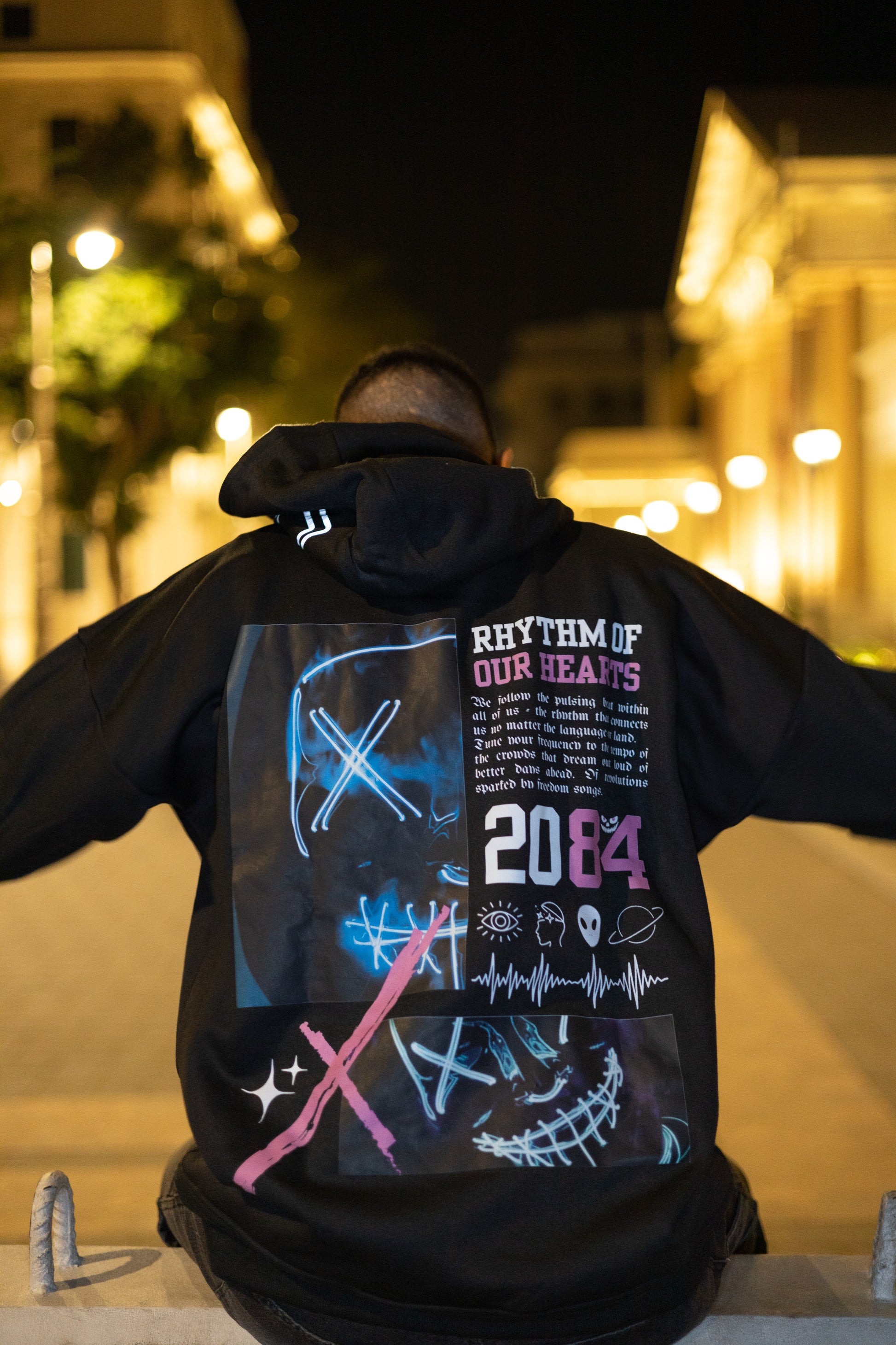 Signature black hoodie celebrating cultures and communities that move us with subtle reflective musical details and bold "Rhythm of Our Hearts" title graphic.